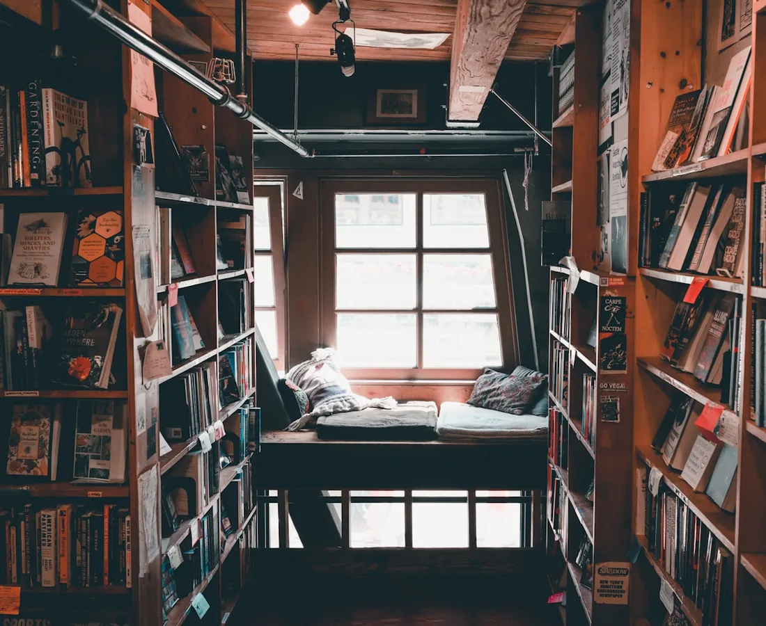 Deckenhohe Bibliothek aus dunklem Holz mit Leseplatz am Fenster